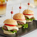 Front of the House red bamboo ball picks in a group of mini burgers on a black plate.