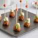 A plate of meatballs on Front of the House orange bamboo ball picks with cheese and greens.