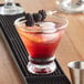 A drink with blackberries and a white bamboo ball pick on a bar.