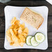 A Milano white square melamine plate with a sandwich and chips on it.