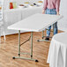 A woman standing next to a Lancaster Table & Seating granite white plastic folding table.