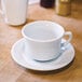A close-up of a Tuxton white saucer with an embossed rim with a white cup on it.
