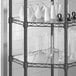 A Regency black metal corner shelf with a clear PVC liner holding vases and glasses.