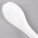 A white plastic WNA Comet Asian soup spoon on a gray surface.