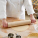 A person rolling out dough with a Choice wood rolling pin on a wooden board.