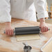 A person using a Choice stainless steel rolling pin to roll out dough on a table.