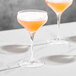 Three Della Luce Astro Coupe glasses with pink and orange cocktails on a marble counter.