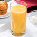 A Libbey customizable cooler glass filled with orange juice sits on a table next to a muffin.