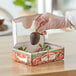 A person in gloves holding a 1/2 lb. chocolate covered strawberry in a windowed box.