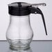 A Tablecraft clear glass syrup dispenser with a black handle.
