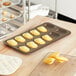 A Gobel Madeleine pan with yellow madeleines on a wooden surface.