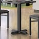 A black Lancaster Table & Seating column table base with a cup on it.