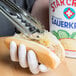 A person using tongs to hold a Star Cross Sauerkraut-covered hot dog.