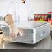 A chef in gloves using a Vollrath aluminum double roaster pan on a counter.