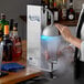 A woman using an Avantco Countertop Glass Froster to chill a glass for a drink.