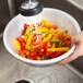 A person using a Thunder Group aluminum colander to rinse a bowl of colorful peppers.
