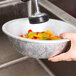 A hand holding a Thunder Group aluminum colander filled with mixed vegetables over a bowl.