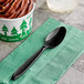 A black Solo Impress plastic teaspoon on a green napkin with a cup of chocolate ice cream.