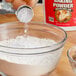 A person pouring baking powder into a bowl of flour.