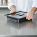 A chef holding a black plastic container with a black Cambro lid.