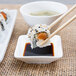 A sushi roll with chopsticks over a white square plate with American Metalcraft white square porcelain sauce cup filled with soy sauce.