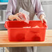 A woman holding a bag of meat in a red Vigor bus tub on a counter in a professional kitchen.