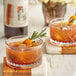 Two glasses of DaVinci Gourmet Old Fashioned drinks with rosemary and orange slices on a white and wood surface.