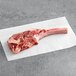 A raw TenderBison bone-in bison tomahawk ribeye steak on white paper.