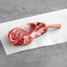 A raw TenderBison bone-in ribeye steak on white paper.
