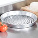 An American Metalcraft Super Perforated Pizza Pan on a table with tomatoes and a ball of dough.