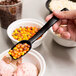 A hand holding a Carlisle black salad bar spoon with candy in it.