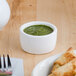 A plate of food with a Tuxton white ramekin of green sauce on a table.