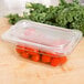 A Carlisle clear plastic food pan on a counter with tomatoes and kale inside.