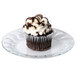 A chocolate cupcake with white frosting on an Arcoroc glass dessert plate.