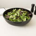 A bowl of salad with red and green leaves in a Cambro black ribbed bowl.