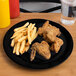 A Carlisle black melamine plate with fried chicken and fries on it.