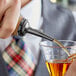 A person using an Acopa black liquor pourer to pour a drink into a glass.