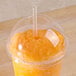 A Fabri-Kal Greenware plastic cup lid with a straw in it over an orange drink.