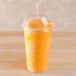 A Fabri-Kal clear plastic dome lid on a plastic cup filled with a yellow liquid with a straw.
