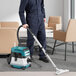 A man in blue overalls using a Makita cordless wet/dry vacuum to clean the floor.