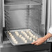 A person putting cookies in a Delfield tray rack in an oven.