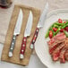 A plate with steak and vegetables on a napkin next to an Acopa steak knife with a natural finish pakkawood handle.