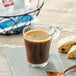 A glass cup of illy decaf coffee on a table with a biscuit.