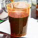 A Fineline Savvi Serve tall neon orange plastic tumbler filled with brown liquid on a table.