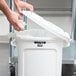 A person's hands putting a white Rubbermaid lid on a white plastic trash can.