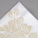 A white Hoffmaster linen-like dinner napkin with a gold flower design.