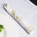 A fork wrapped in a Hoffmaster Gold Prestige linen-like dinner napkin next to a plate of green beans.