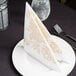 A white plate with a gold linen-like napkin folded on it next to a fork and knife.