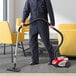 A person in a uniform using an Atrix Lil' Red canister vacuum to clean a chair.