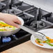 A hand using Choice stainless steel utility tongs to serve food onto a plate.